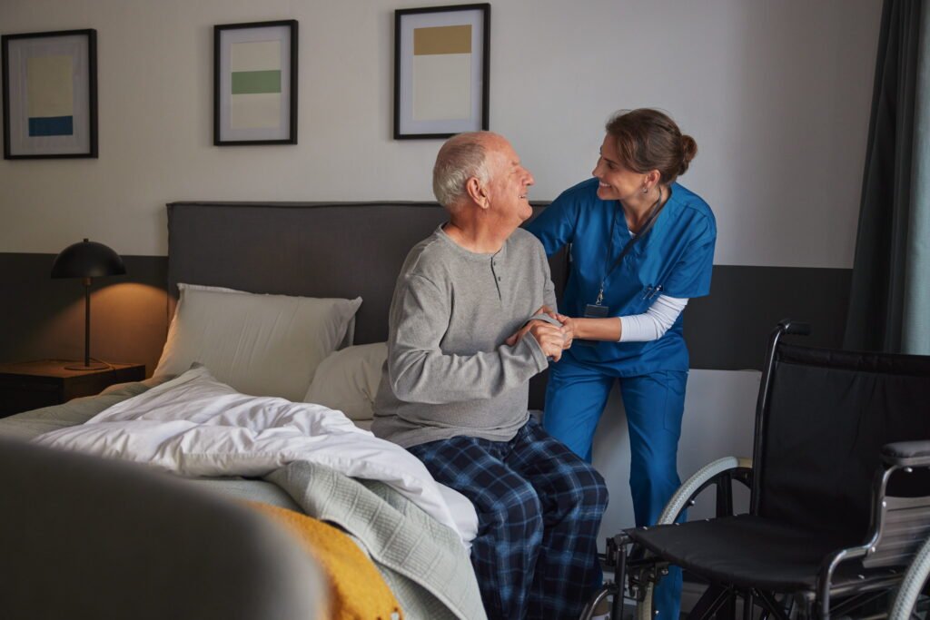Smiling nurse assisting disabled senior man to get up from bed